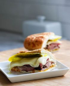 a sandwich with meat and cheese is on a white plate next to a bread roll