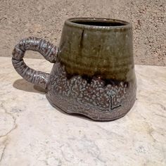 a brown and black mug sitting on top of a marble counter next to a wall