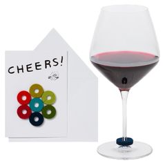 a glass of red wine next to a card with the word cheers