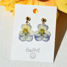 a pair of blue and white flower earrings sitting on top of a card next to a yellow flower