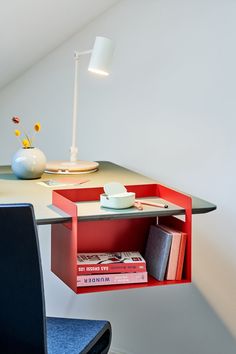 a desk with a lamp and some books on it in a room that has white walls