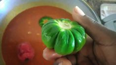 a person holding a green pepper in a bowl of soup