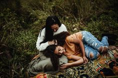 two women are laying on a blanket in the grass and one is holding her head