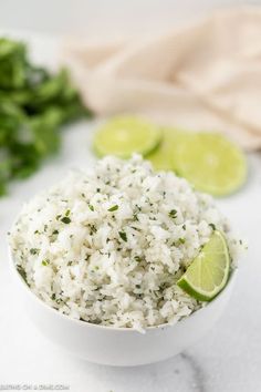 a white bowl filled with rice, limes and cilantro on a table