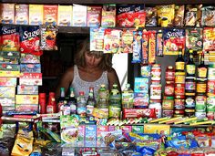 a woman standing in front of a store filled with lots of food and drink bottles