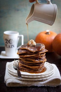 a stack of pancakes on a plate with syrup being drizzled over them