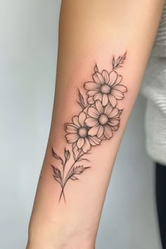 Forearm tattoo of three intricate, black and grey flowers with leaves. Flower Tattoo Designs For Women Arm, Narcissus And Daisy Flower Tattoo, Daisy Sweet Pea Tattoo, Fine Line Daisy Tattoo, Daisies Tattoo, Daisy Tattoo Ideas, Daisy Tattoos, Sweet Pea Tattoo, Daisy Tattoo Designs