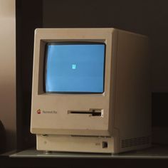 an old apple computer sitting on top of a desk in front of a wall with a small window