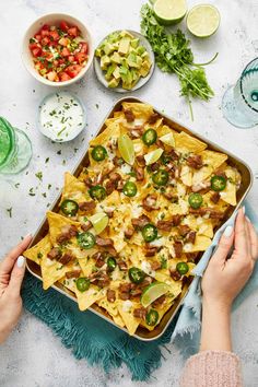 a person holding a tray filled with nachos next to bowls of salsa and lime wedges