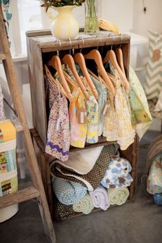 a wooden shelf filled with clothes next to a vase full of flowers on top of a table