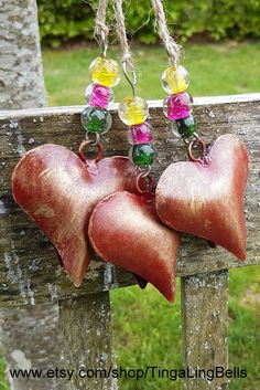 two red hearts hanging from a wooden fence with glass bead earrings attached to them