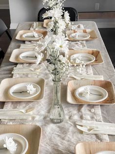 the table is set with white flowers in a vase, plates and napkins on it