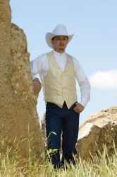 a man wearing a white hat and vest standing next to a large rock in the grass