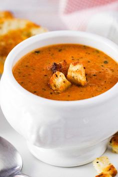 a white bowl filled with roasted tomato basil soup and croutons on the side