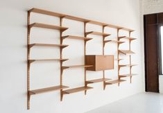 a wall mounted book shelf next to a window in an empty room with white walls