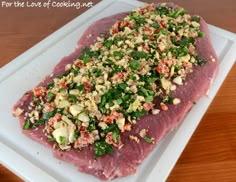 raw meat on a white plate with chopped vegetables and seasoning sprinkles