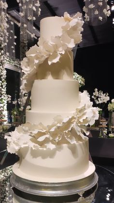 a three tiered white wedding cake with flowers on the top and bottom, sitting on a glass table