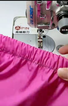 someone using a sewing machine to sew pink material