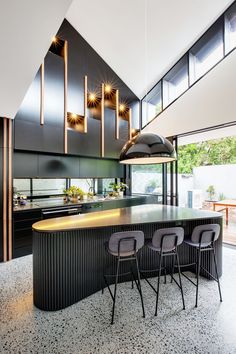 a kitchen with an island and three chairs in it, along with lights hanging from the ceiling