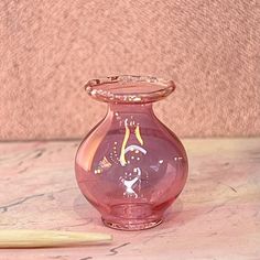 a pink glass vase sitting on top of a table next to a wooden pencil holder