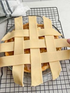 a pie sitting on top of a cooling rack next to a person's hand