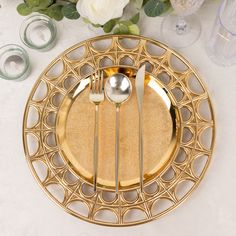 a gold plate with two forks and spoons on it next to some white flowers