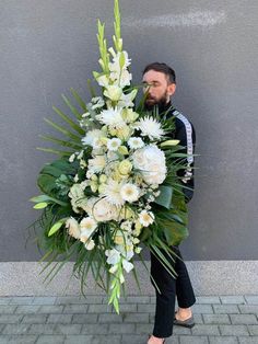 a man holding a large bouquet of white flowers and greenery in front of a gray wall