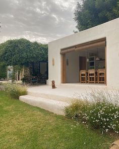 a dog is sitting on the grass in front of a house with an open patio