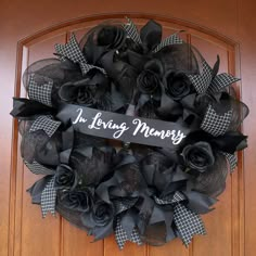 a wreath that says in loving memory with black roses on the front door and plaid ribbon