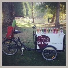 a bike with a cart attached to it parked in the grass next to a tree