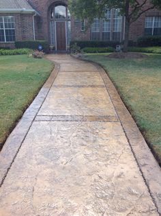 a sidewalk in front of a house with grass and bushes on either side of it