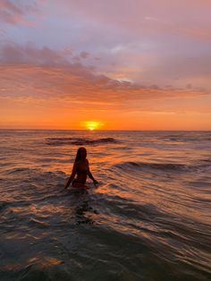 a woman sitting in the ocean at sunset