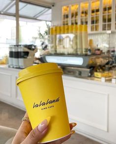 a woman holding up a yellow coffee cup in front of a restaurant counter with food on it