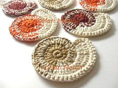 six crocheted coasters are arranged on a white table top with orange and red designs