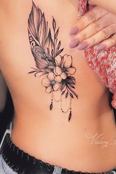 a woman's stomach with a feather and flowers tattoo on her side ribcage