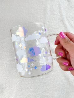 a hand holding a clear cup with clouds and stars on the outside, in front of a white background