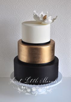 a three tiered cake with white and black frosting on the top, topped with a flower