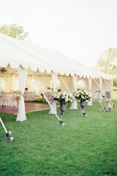 a large white tent set up with chairs and flowers in vases on the grass