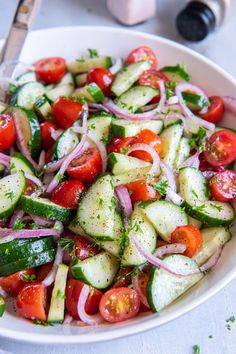 a white bowl filled with cucumber, tomatoes and onions next to a fork