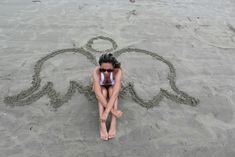 a woman sitting in the sand with an elephant drawn on it