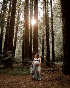 a pregnant woman standing in the middle of a forest with sun shining through the trees