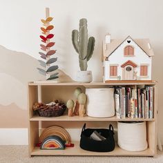 a book shelf with books, toys and other items on it next to a cactus