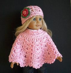 a doll is wearing a pink knitted ponchy with a flower on it