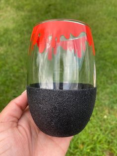 a hand holding up a wine glass with red and green paint on it in the grass