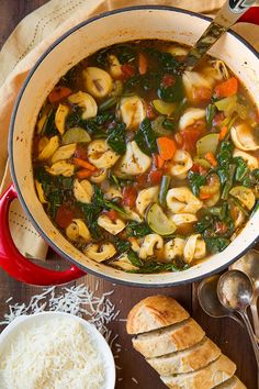 a pot filled with pasta and vegetable soup next to bread on a wooden table top