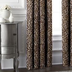 a leopard print curtain hanging in front of a window with a white vase next to it