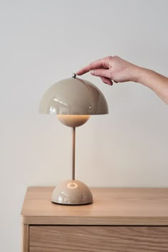 a person's hand reaching for an object on top of a table with a lamp