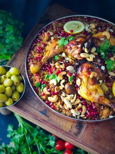 a large pan filled with food next to olives and lemon wedges on a cutting board