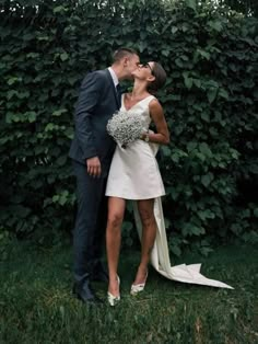 a bride and groom kissing in front of a hedge