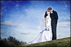 a bride and groom kissing on the top of a hill with blue skies in the background